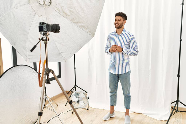 Hombre joven árabe haciéndose pasar por modelo en el estudio de fotografía manos juntas y dedos cruzados sonriente relajado y alegre. éxito y optimismo  - Foto, Imagen