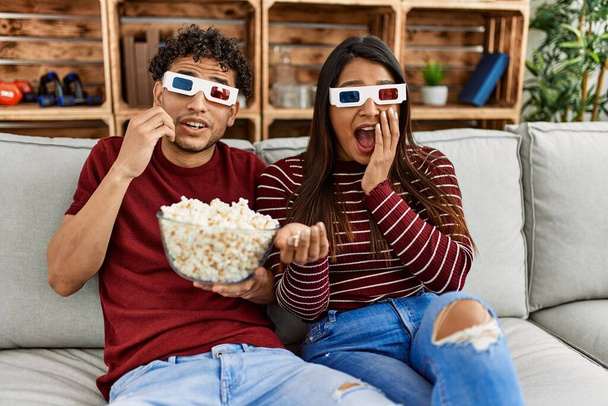 Jeune couple latin effrayé regarder un film en utilisant des lunettes 3D à la maison. - Photo, image