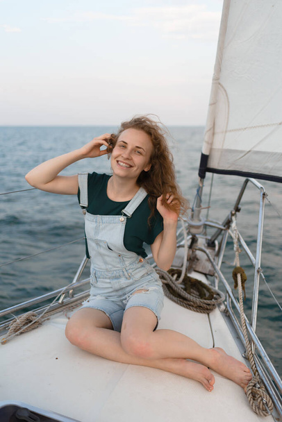 魅力的な若い女性がヨットに座って海の旅を楽しんでいます。旅行、観光、夏のコンセプト - 写真・画像