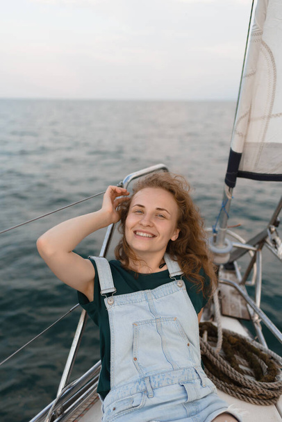 Atraktivní žena se dívá do kamery a dotýká se zrzavých vlasů, ležících na jachtě. Cestování, cestovní ruch a letní koncepce - Fotografie, Obrázek