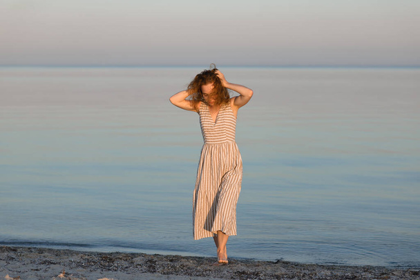 A red-haired woman is walking on the beach with a strong wind. High-quality photo - Fotó, kép