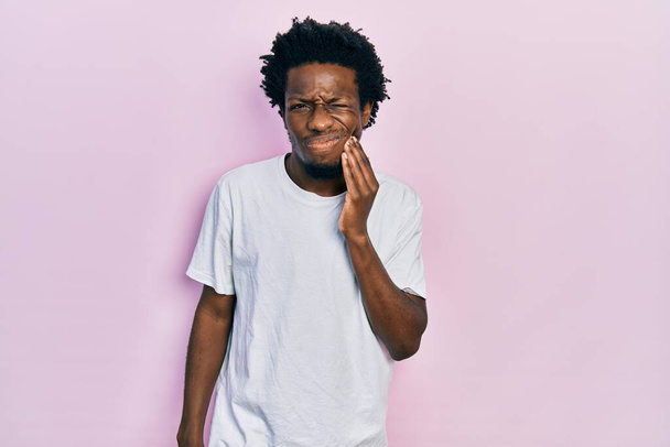 Sıradan beyaz tişörtler giyen genç Afro-Amerikan bir adam diş ağrısı ya da diş hastalığından dolayı ağızlarına acı dolu bir ifadeyle dokunuyor. dişçi  - Fotoğraf, Görsel