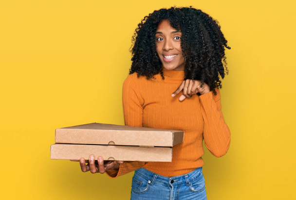 Joven africana americana chica sosteniendo entrega pizza caja sonriendo feliz apuntando con la mano y el dedo  - Foto, imagen
