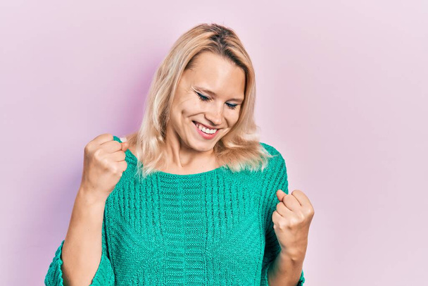 Hermosa mujer rubia caucásica con suéter de invierno casual celebrando sorprendida y sorprendida por el éxito con los brazos levantados y los ojos cerrados  - Foto, imagen