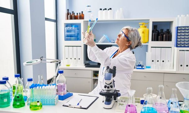 Женщина средних лет в форме ученого, похожая на пробирки в лаборатории - Фото, изображение