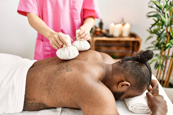 Young african american man having back massage with thai bags at beauty center - Фото, изображение