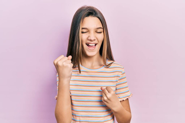 Jeune fille brune portant t-shirt à rayures décontractées célébrant surpris et étonnés pour le succès avec les bras levés et les yeux fermés  - Photo, image