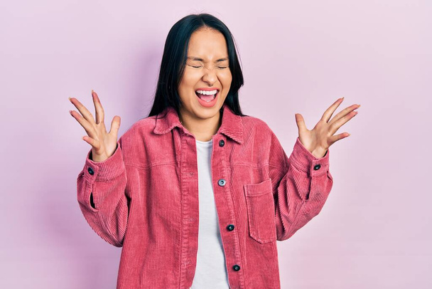 Beautiful hispanic woman with nose piercing wearing casual pink jacket celebrating mad and crazy for success with arms raised and closed eyes screaming excited. winner concept  - Foto, Imagen