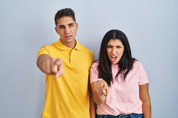Jeune couple debout sur fond isolé pointant mécontent et frustré à la caméra, en colère et furieux contre vous  - Photo, image