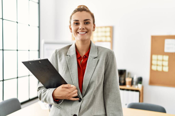 Junge Geschäftsfrau lächelt selbstbewusst und hält Klemmbrett im Büro - Foto, Bild