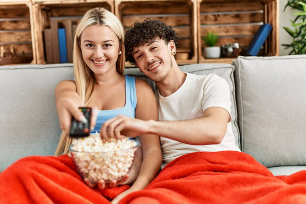 Mladý pár sleduje film a jíst popcorn sedí na pohovce doma. - Fotografie, Obrázek