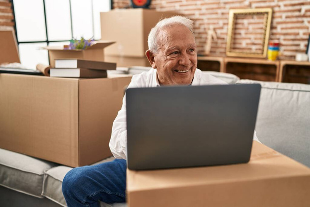 Senior man smiling confident using laptop at new home - Photo, Image