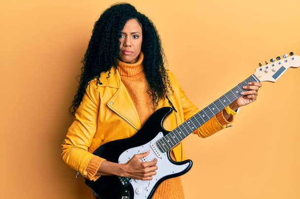 Mujer afroamericana de mediana edad tocando la guitarra eléctrica relajada con expresión seria en la cara. simple y natural mirando a la cámara.  - Foto, Imagen