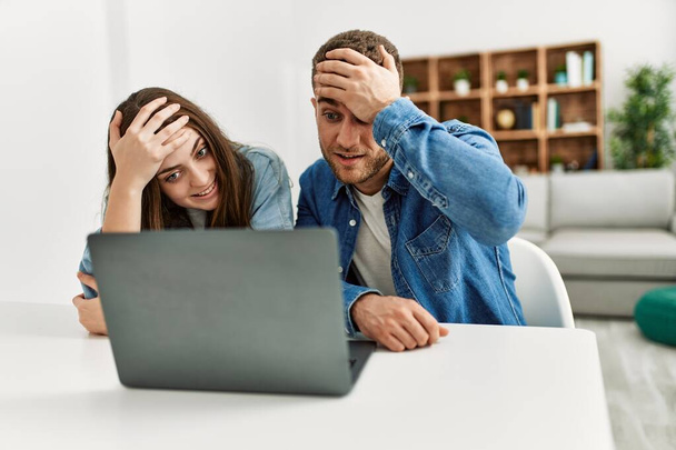 Young caucasian couple working using computer laptop at home stressed and frustrated with hand on head, surprised and angry face  - Foto, immagini