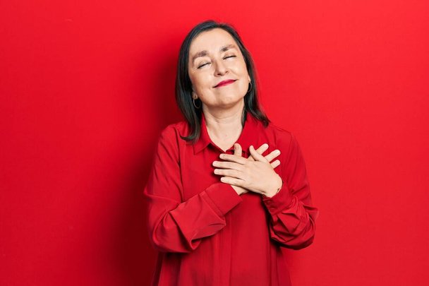 Middle age hispanic woman wearing casual clothes smiling with hands on chest with closed eyes and grateful gesture on face. health concept.  - Фото, зображення