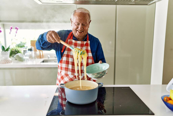 Senior man smiling confident cooking spaghetti at kitchen - 写真・画像