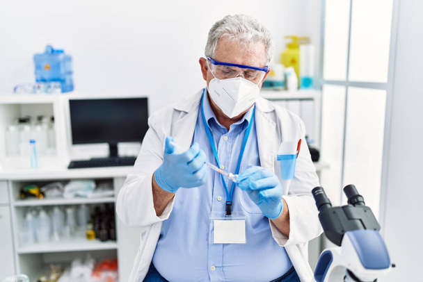 Middle age grey-haired man wearing scientist uniform using syringe at laboratory - Foto, Imagen