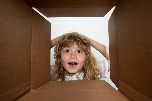 The surprised child unpacking, opening carton box and looking inside. The package, delivery, surprise, kids gift concept. Open box and delivery parcel for children. - Photo, Image