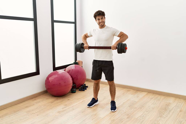 Young hispanic man smiling confident training with dumbbell at sport center - Fotó, kép
