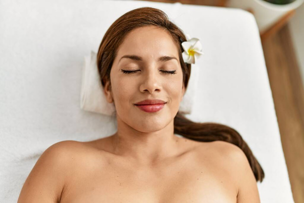 Joven latina sonriendo confiada relajada acostada sobre mesa de masaje  - Foto, imagen