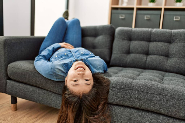 Young chinese girl smiling happy lying on the sofa at home. - Photo, Image
