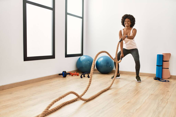 Молода афроамериканська жінка, яка посміхається з упевненістю тренується з бойовою мотузкою в спортивному центрі. - Фото, зображення