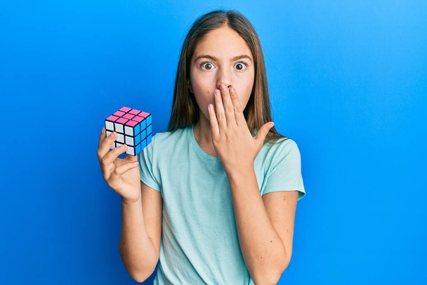 Bella bruna bambina che gioca colorato puzzle cubo intelligenza gioco che copre la bocca con la mano, scioccato e spaventato per errore. espressione sorpresa  - Foto, immagini