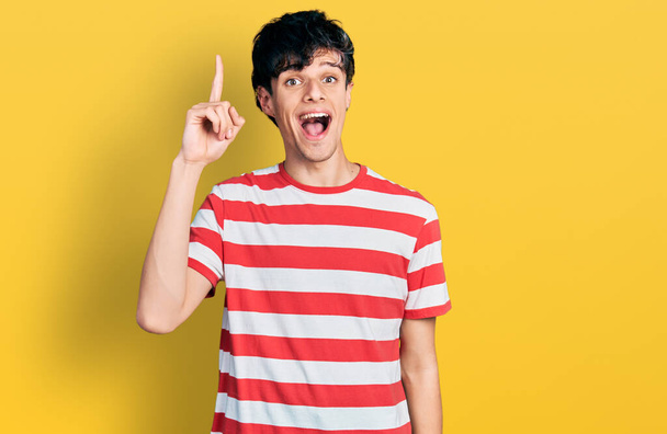 Handsome hipster young man wearing casual striped t shirt pointing finger up with successful idea. exited and happy. number one.  - Photo, Image