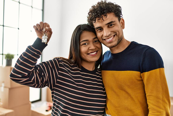 Young latin couple smiling happy and hugging holding key of new home. - Foto, afbeelding