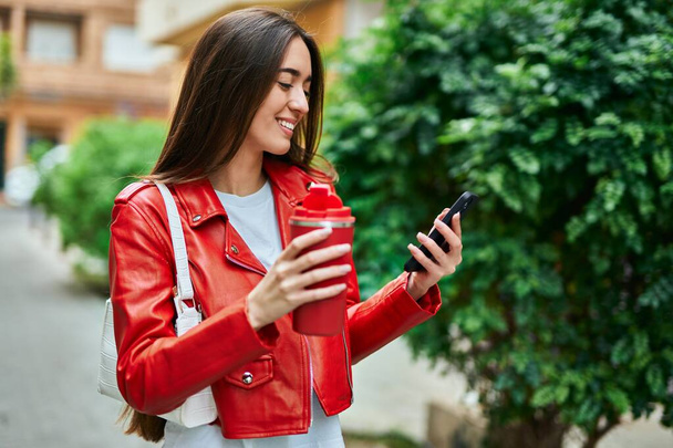 Молода іспаномовна жінка використовує смартфон і п'є каву в місті
. - Фото, зображення