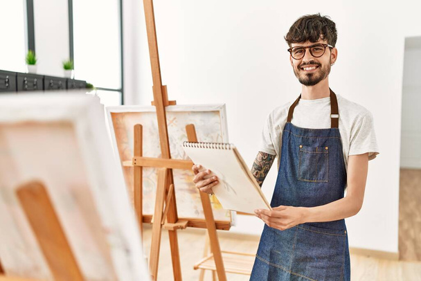 Молодий іспаномовний художник посміхається щасливим малюнком в художній студії
. - Фото, зображення