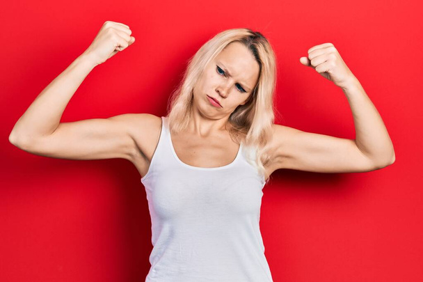 Hermosa mujer rubia caucásica con camiseta blanca casual que muestra los músculos de los brazos sonriendo orgulloso. concepto de fitness.  - Foto, imagen