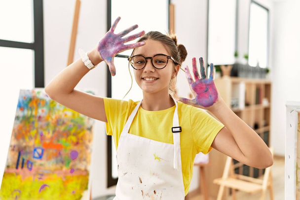 Adorable girl smiling confident showing painted palm hands at art studio - Foto, Imagem