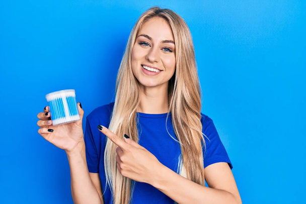 Young caucasian woman holding earwax cotton removers smiling happy pointing with hand and finger  - Foto, imagen