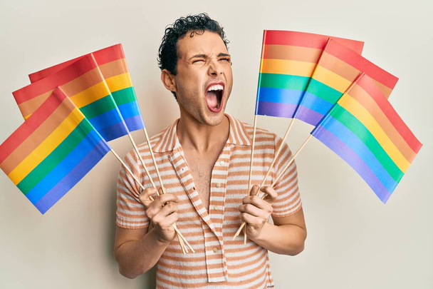 Knappe man draagt make-up met regenboog lgbtq vlaggen boos en gek schreeuwen gefrustreerd en woedend, schreeuwen van woede. woede en agressief concept.  - Foto, afbeelding