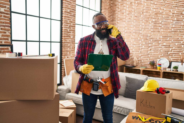 Jovem afro-americano homem trabalhador falando no smartphone em nova casa - Foto, Imagem