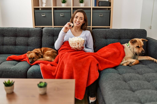 Young hispanic woman watching movie sitting on sofa with dogs at home - Photo, Image