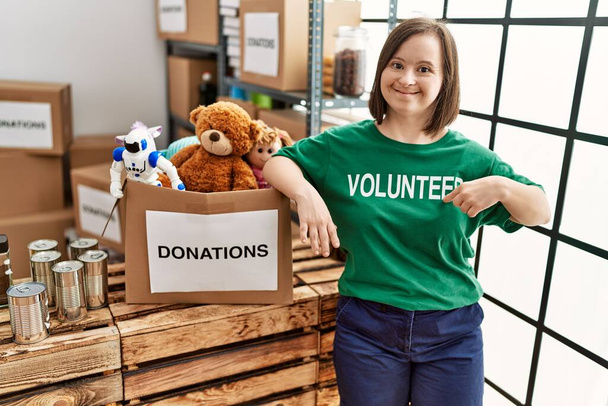 Femme brune avec le syndrome du duvet debout par boîte avec des jouets donnés au stand de dons - Photo, image