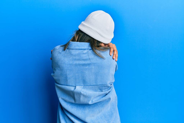 Young latin woman wearing cute wool cap hugging oneself happy and positive from backwards. self love and self care  - Foto, Imagen