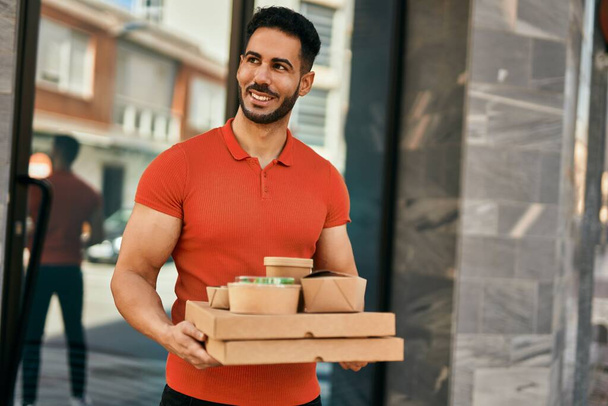 Fiatal spanyol férfi mosolyog boldog gazdaság elvenni az ételt a városban. - Fotó, kép