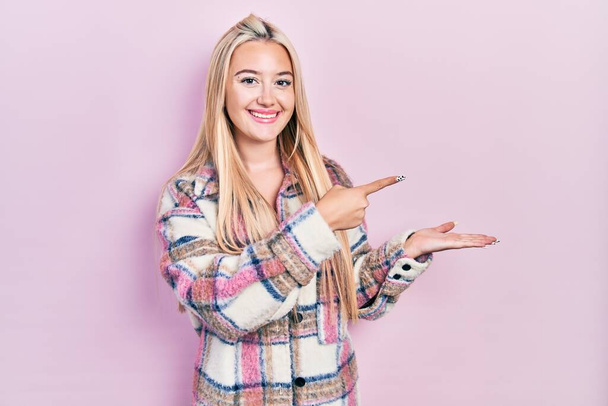 Menina loira jovem vestindo roupas casuais espantado e sorrindo para a câmera ao apresentar com a mão e apontando com o dedo.  - Foto, Imagem