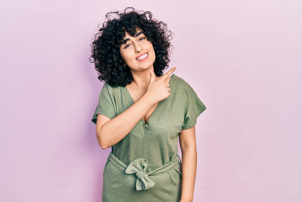 Young middle east woman wearing casual clothes cheerful with a smile of face pointing with hand and finger up to the side with happy and natural expression on face  - Foto, imagen