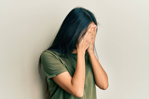 Giovane ragazza ispanica indossa maglietta casual con espressione triste che copre il viso con le mani mentre piange. concetto di depressione.  - Foto, immagini