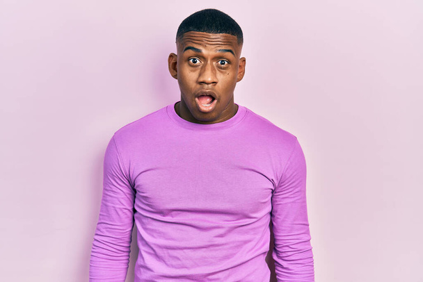 Fiatal fekete férfi visel alkalmi rózsaszín pulóver fél és megdöbbent a meglepetés és csodálkozó kifejezés, félelem és izgatott arc.  - Fotó, kép