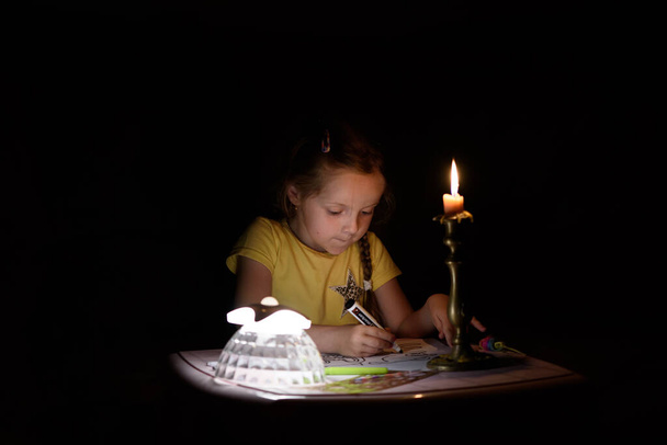 Dívka kreslí fantazie postavy blízko svíčky v tmavé místnosti. Dítě dělá oblíbenou věc během výpadku proudu. - Fotografie, Obrázek