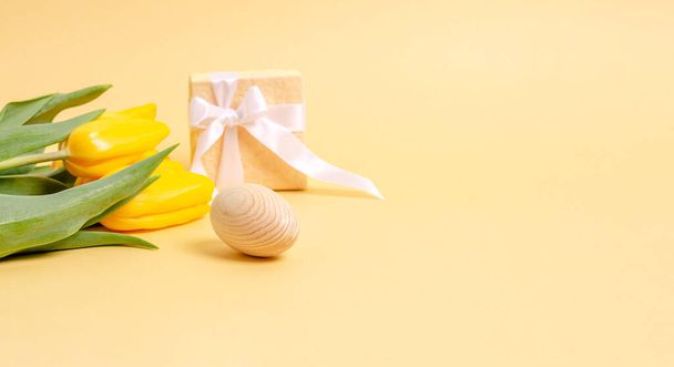 Easter wooden egg, gift box and a bouquet of tulips on a yellow background. - Fotografie, Obrázek