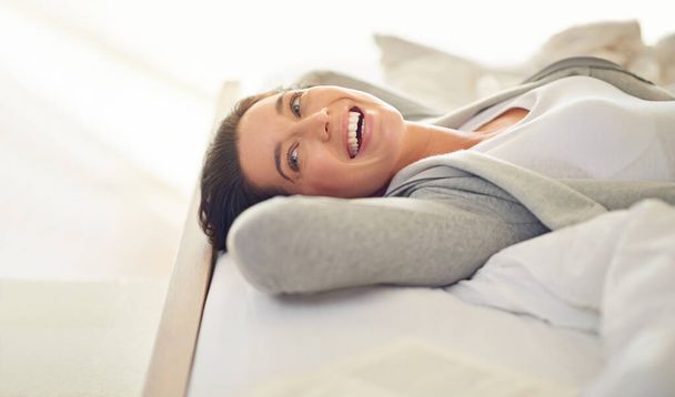 Totally loving this weekend. Cropped shot of a young woman laughing while lying on her bed. - Foto, immagini