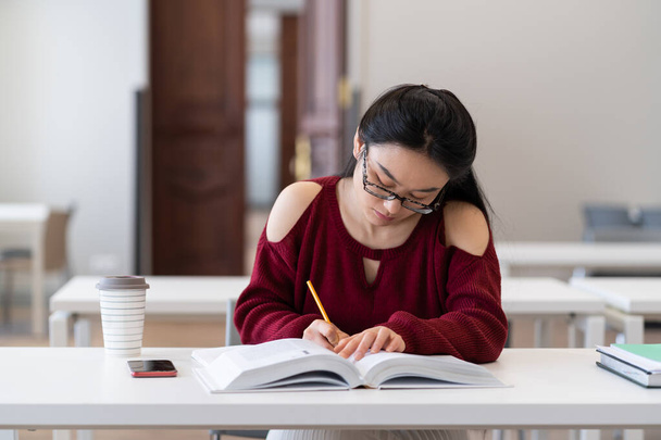 Slim aziatisch meisje schrijven schets tijdens de voorbereiding voor examen in de leeszaal of klas - Foto, afbeelding