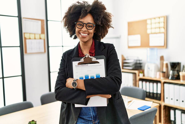 Mladá africká americká žena s úsměvem sebevědomé držení schránky v kanceláři - Fotografie, Obrázek