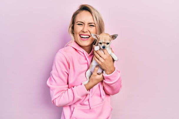 Sarışın, güzel bir kadın sevimli bir chihuahua köpeğine sarılıyor ve kahkahalarla gülüyor..  - Fotoğraf, Görsel